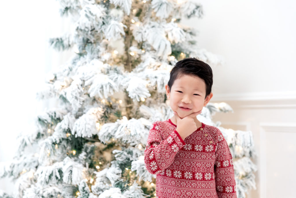 Child in holiday pajama standing in front of a white christmas tree.