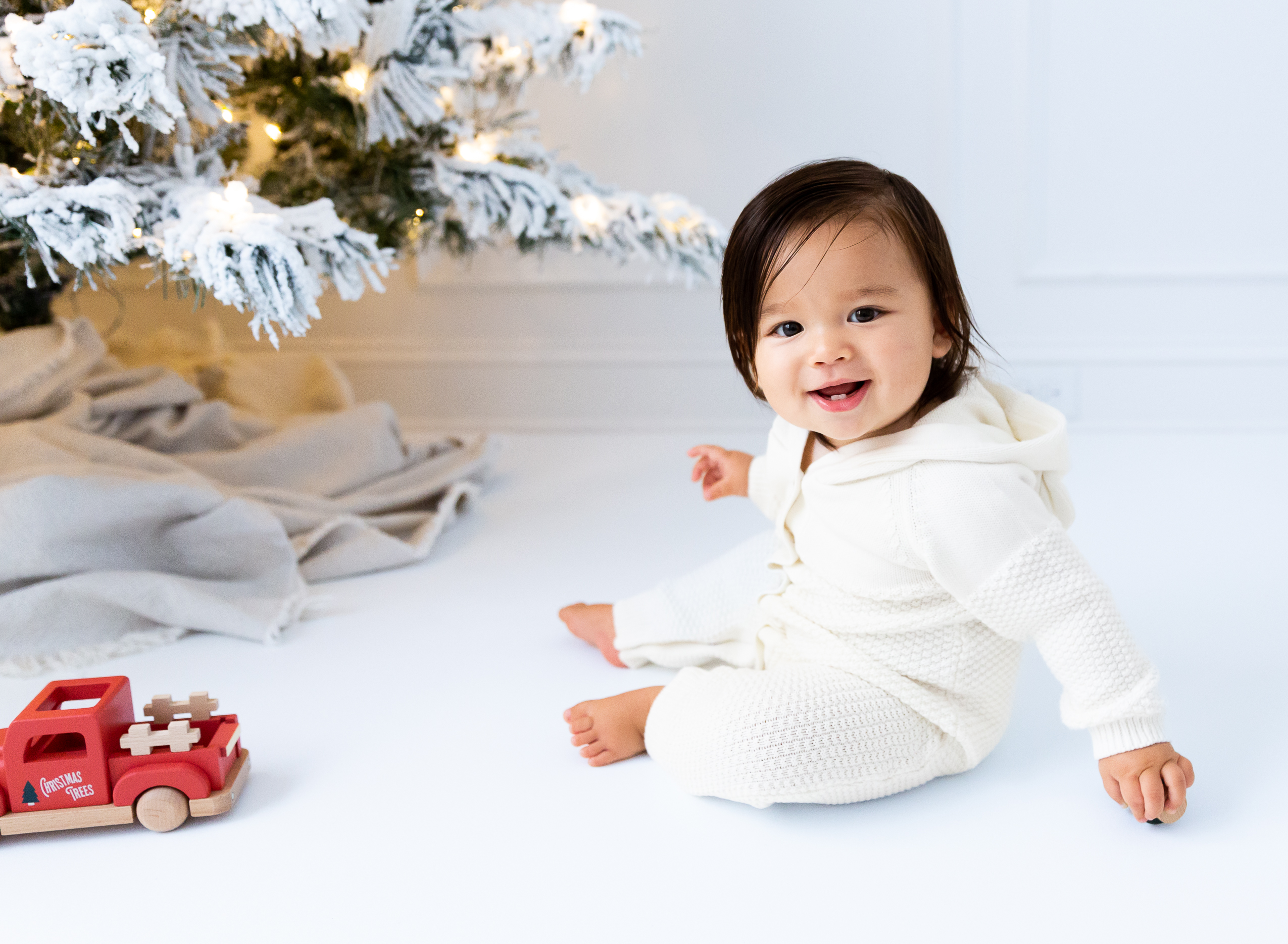 baby sitting near christmas tree all in white and timeless